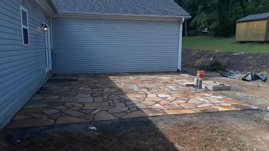 Natural stone patio field in progress beside a residential garage wall, view 6