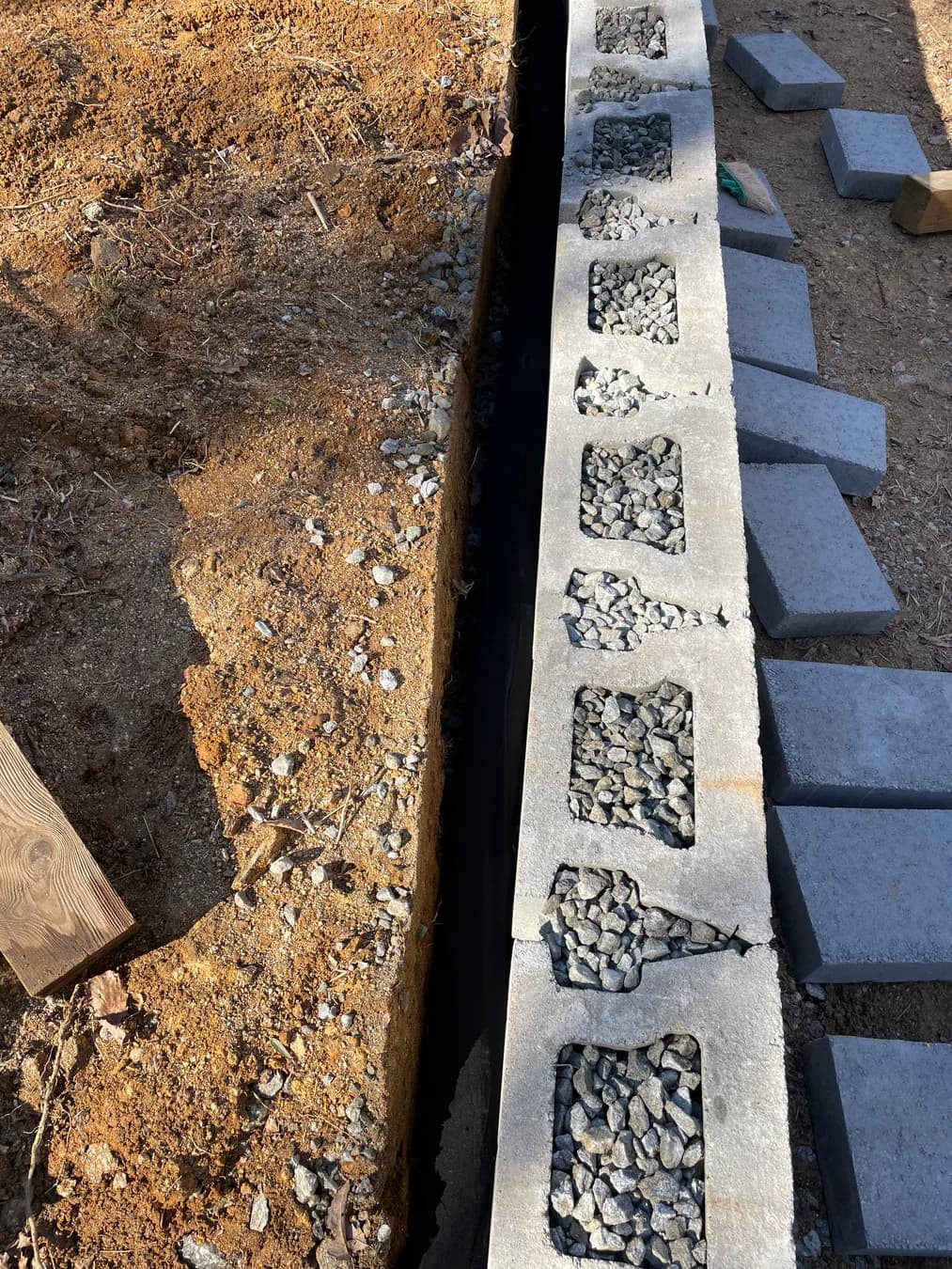 Retaining wall construction with block, drainage stone, and prepared trench, view 1